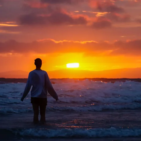 A figure standing in the sea, silhouetted against the sunset